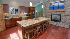 A modern kitchen with a large island, wooden cabinets, granite countertops, and a stone accent wall with a fireplace. - Enormous luxury cabin rental in unbeatable South Tahoe location (South Lake Tahoe)