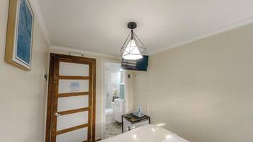A hotel room with a bed, a bedside table, a hanging light fixture, a door, and a bathroom visible through an open door.