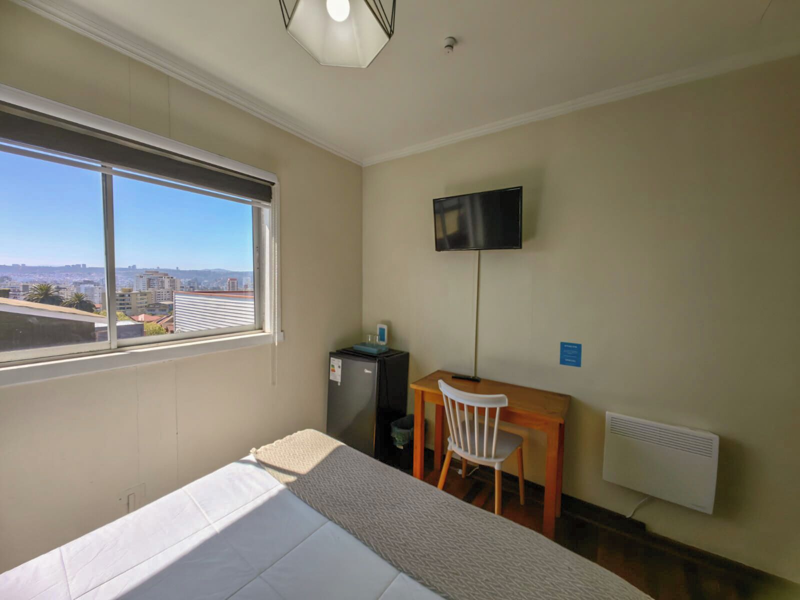 Una habitación de hotel con cama, escritorio, silla, televisor y ventana con vista a la ciudad.