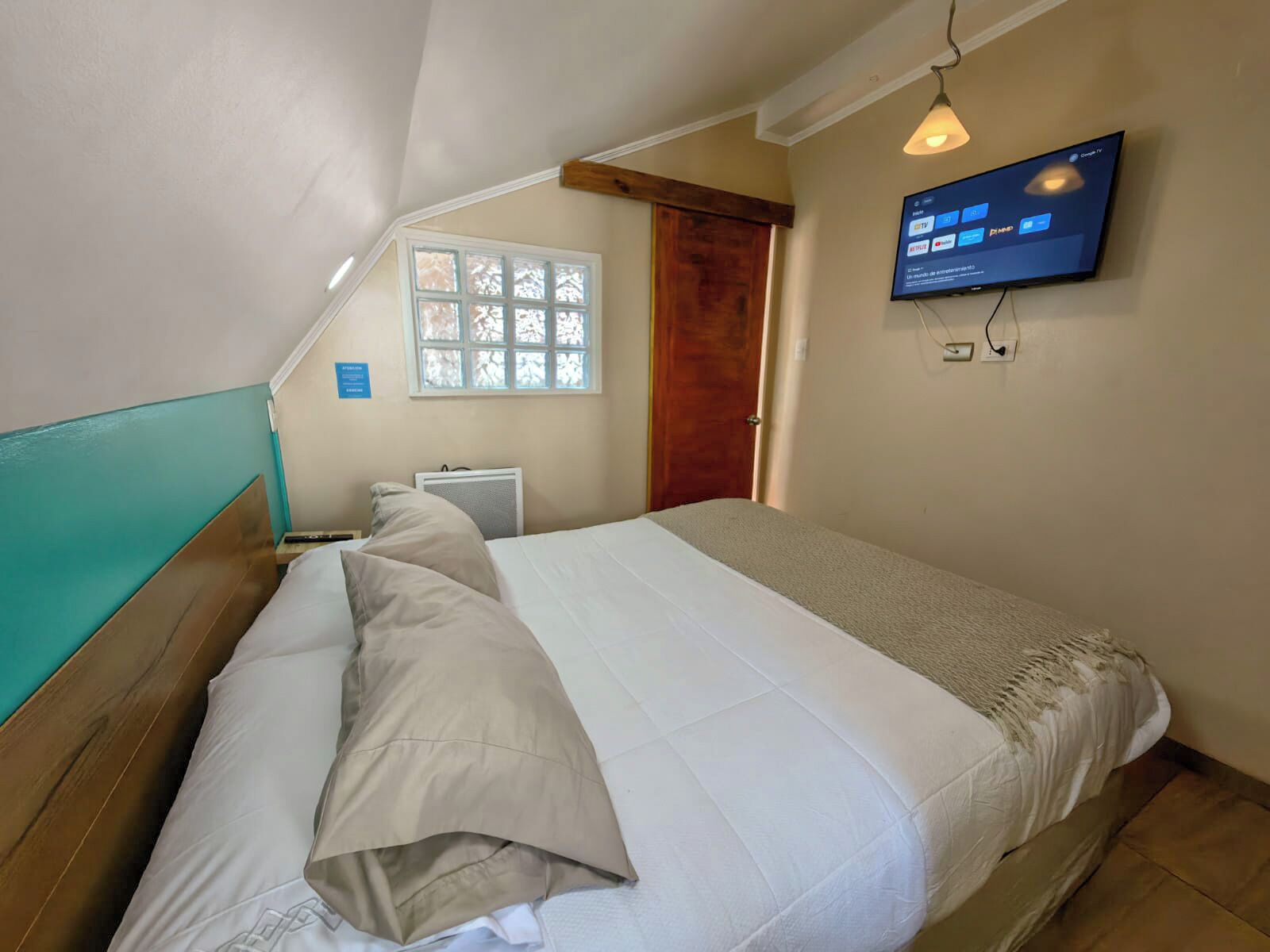 Une chambre à coucher avec un lit, un téléviseur fixé au mur, une fenêtre et une porte.