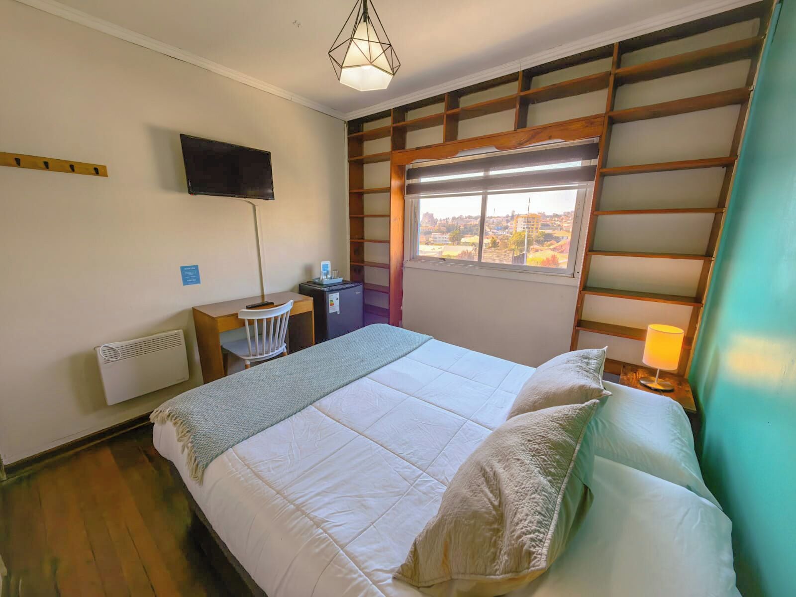 Habitación de hotel con cama, escritorio, silla, televisión, calefactor, ventana con vistas y lámpara.