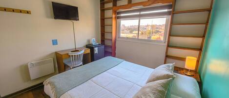 Habitación de hotel con cama, escritorio, silla, televisión, calefactor, ventana con vistas y lámpara.