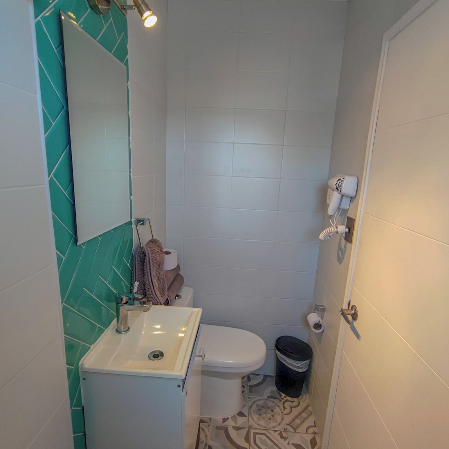 A small bathroom with a white sink, a toilet, and a hairdryer on the wall.