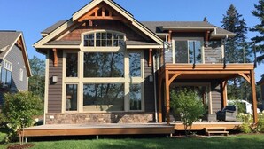 Ein zweistöckiges Haus mit einer großen Veranda, einem Steinfundament und einem überdachten Deck.