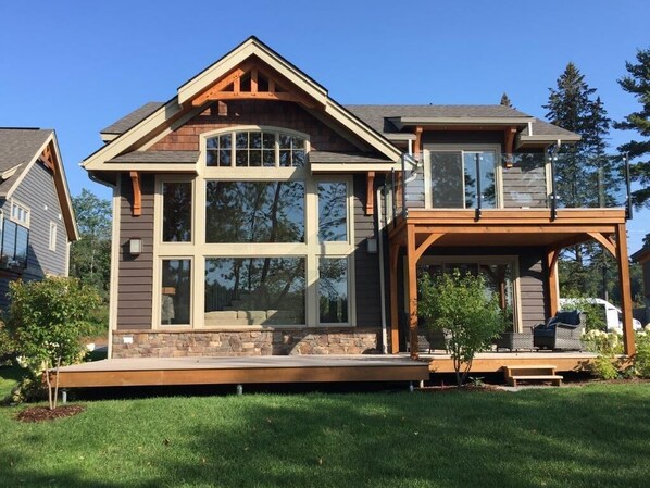 Ein zweistöckiges Haus mit einer großen Veranda, einem Steinfundament und einem überdachten Deck.