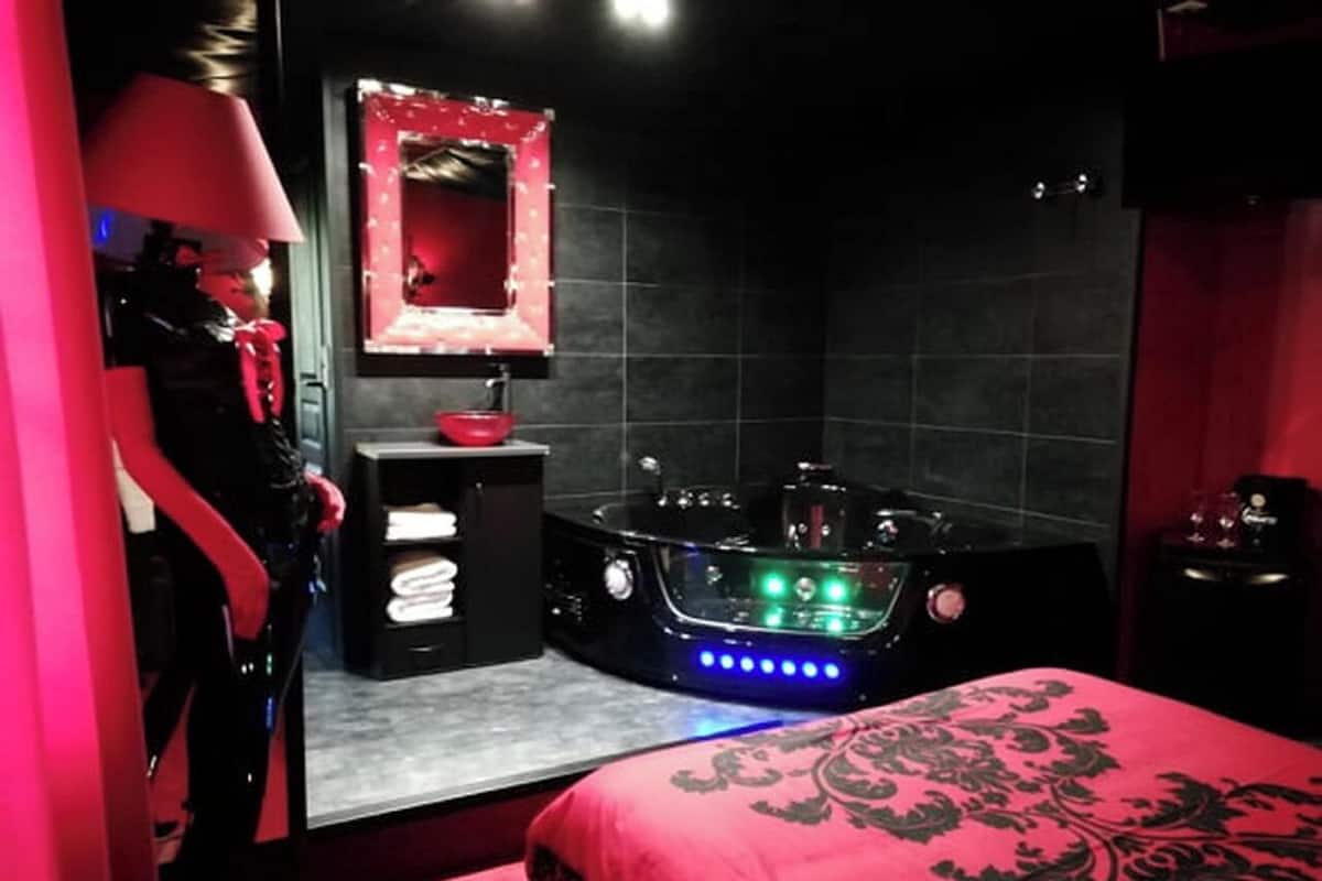A room with a large bathtub, a vanity with a mirror, and a bed with a red bedspread.