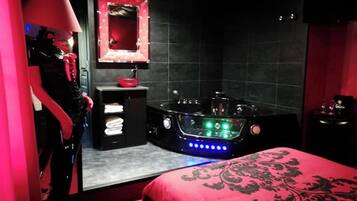 Una habitación con una bañera grande, un tocador con espejo y una cama con colcha roja.