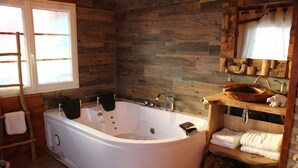 A modern bathroom with a freestanding bathtub, wooden wall paneling, a wooden shelf with towels, and a window with a view. - Sweet-Dreams (Trois-Rivières)