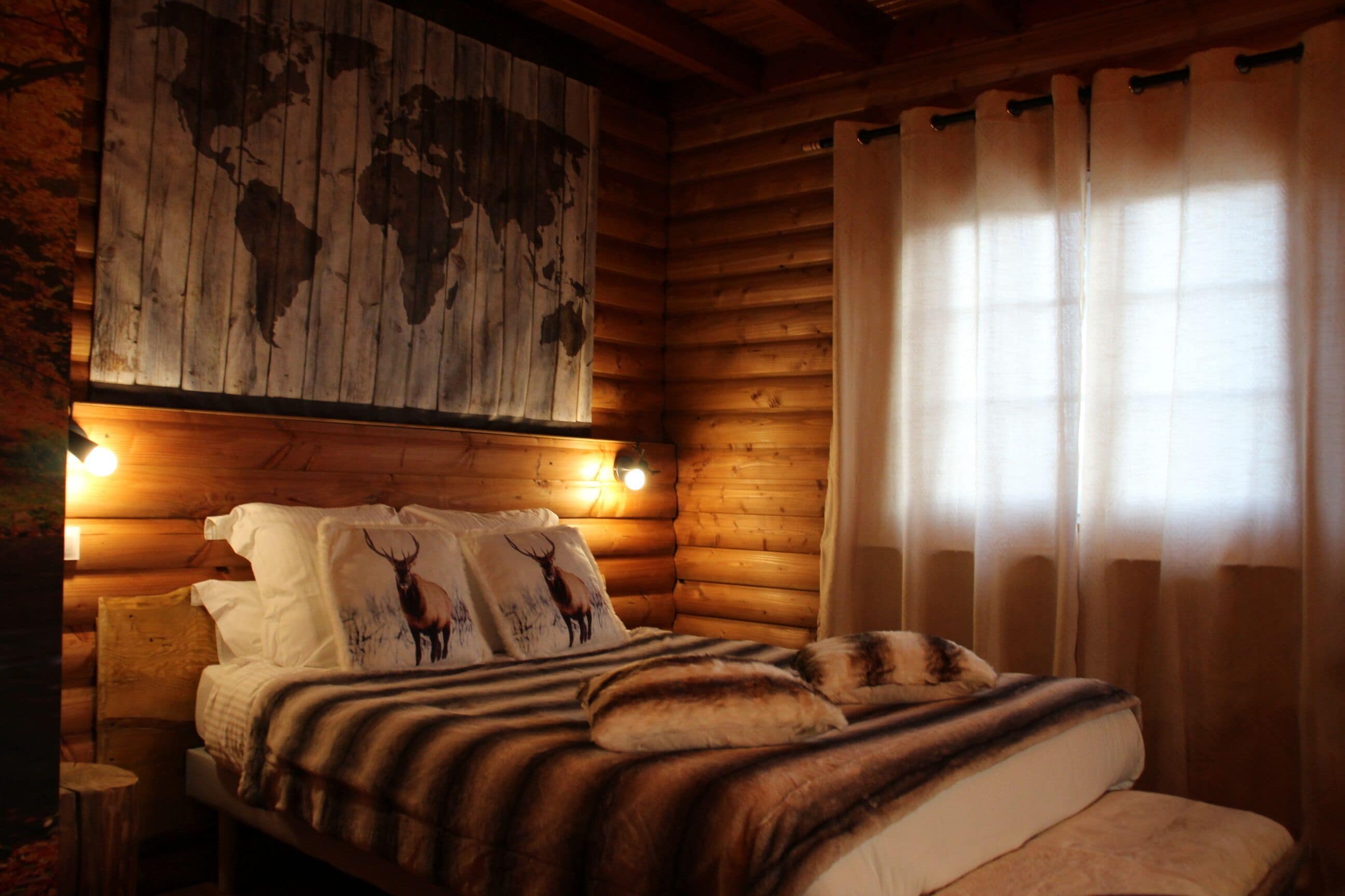 Une chambre chaleureuse dans un chalet en rondins, avec un lit, une carte du monde accrochée au mur et une fenêtre avec des rideaux.