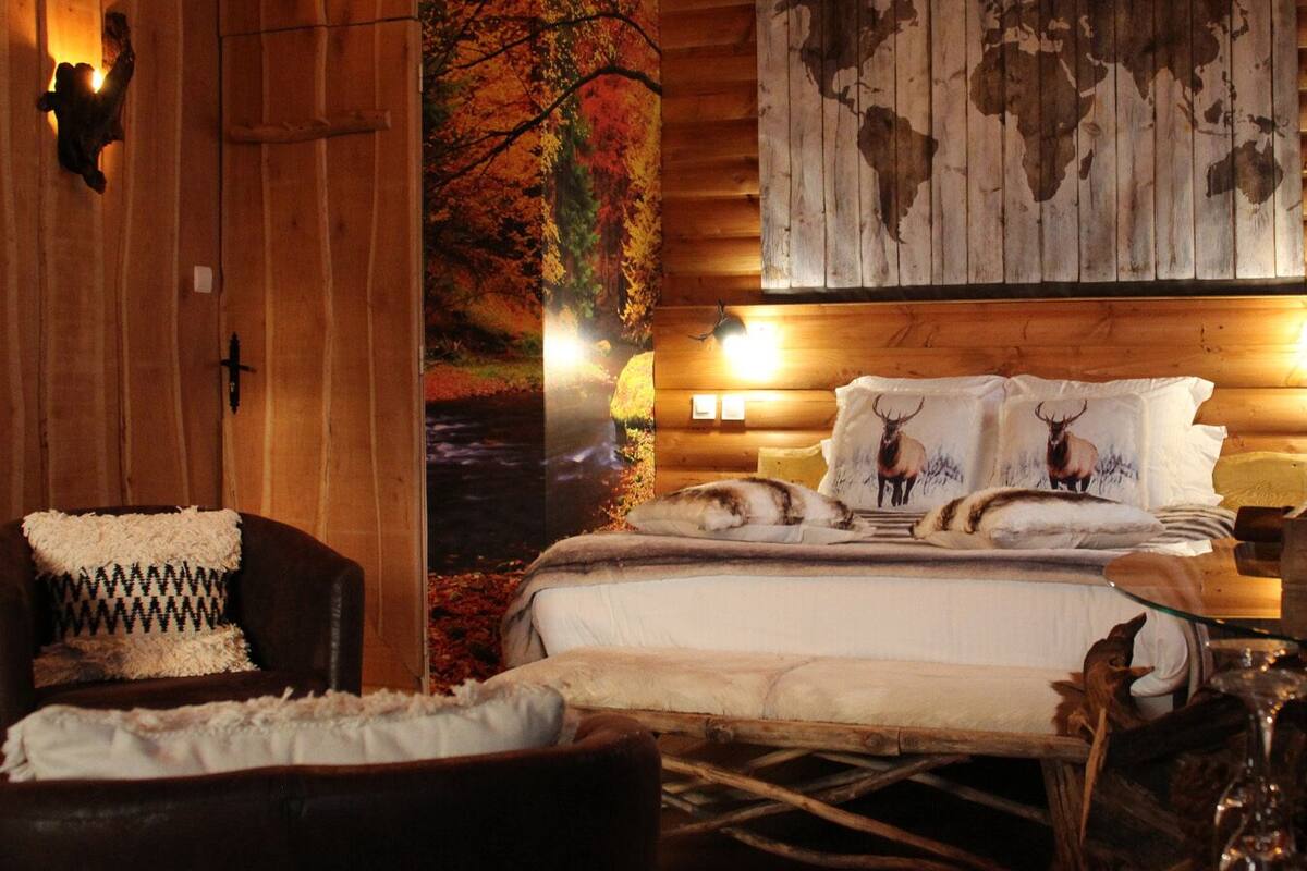 A cozy cabin-style room with a bed, a chair, and a wall mural.