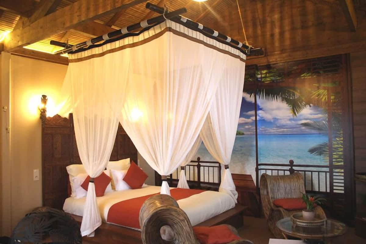 A room with a four-poster bed, a balcony with a view of the sea, and a tropical-themed mural.