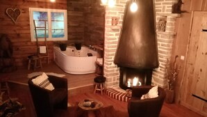 A cozy cabin interior with a stone fireplace, a large bathtub, and rustic wooden walls. - Sweet-Dreams (Trois-Rivières)