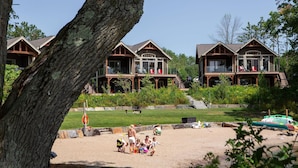 Un complexe hôtelier comprenant plusieurs chalets en bois, une plage de sable et un grand arbre au premier plan.