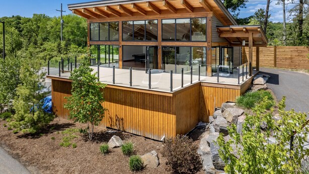 A modern wooden cabin with large glass windows, a deck, and a view of the surrounding forest.