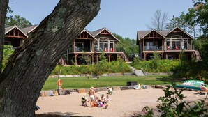 A resort with multiple wooden cabins, a sandy beach area, and a large tree in the foreground.
