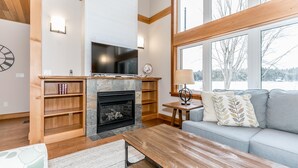 Ein modernes Wohnzimmer mit Kamin, Holzböden, einem Fernseher und einer Couch mit dekorativen Kissen.