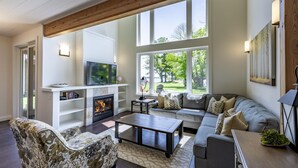 A spacious living room with a fireplace, large windows, a sofa, and a coffee table.