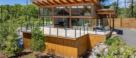 A modern wooden cabin with large glass windows, a deck, and a view of the surrounding forest.
