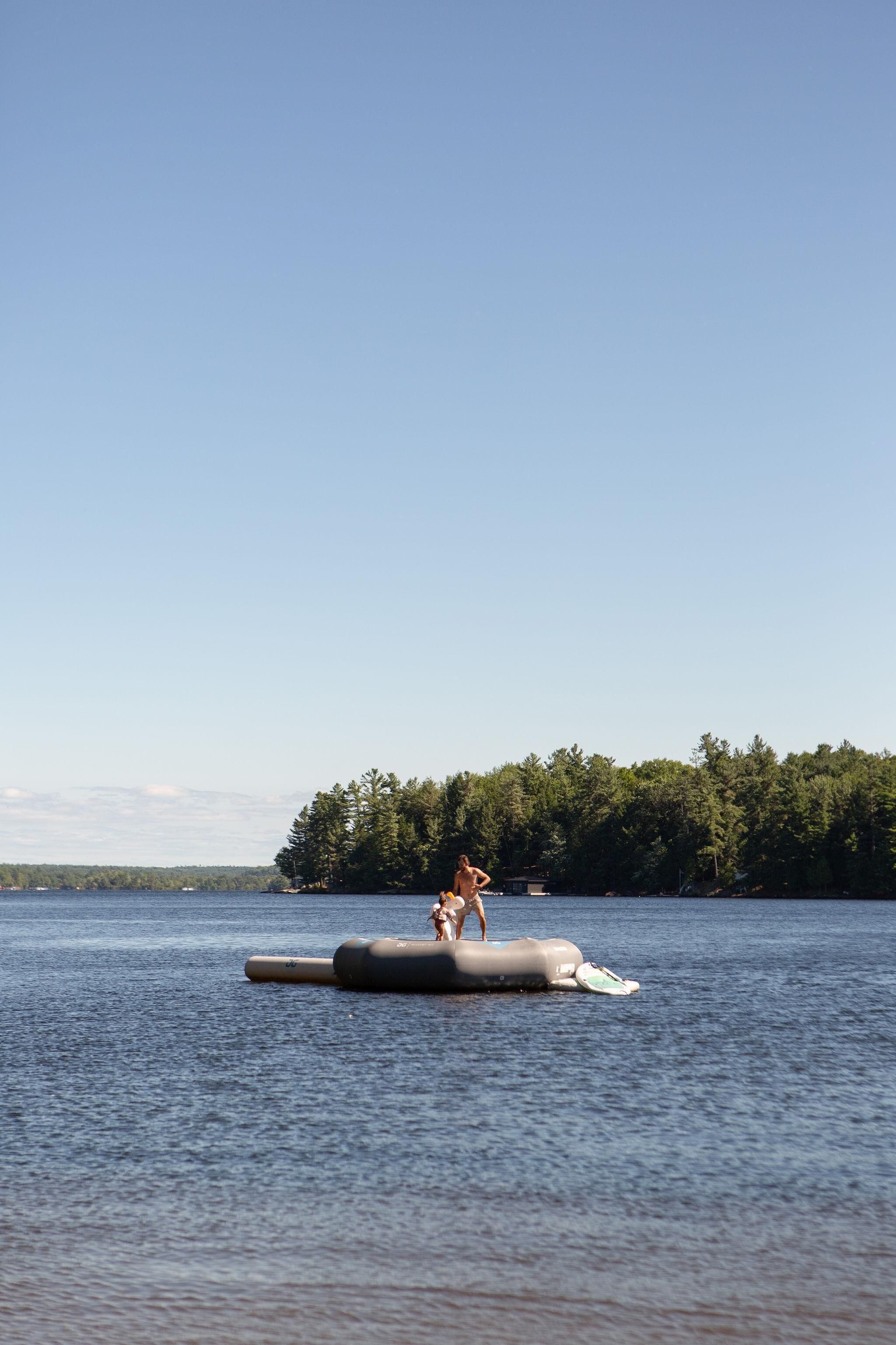 Une personne se tient sur une plateforme flottante, au milieu d’une étendue d’eau, avec une île boisée en arrière-plan.