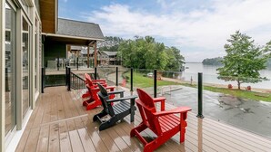 A wooden deck with red and black Adirondack chairs overlooking a body of water.