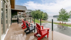 A wooden deck with red and black Adirondack chairs overlooking a body of water. - 4 bed 4 bath Villa on Lake Muskoka (Port Carling)
