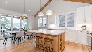 A modern kitchen with a large island, white cabinetry, and a dining area with a wooden table and bar stools. - 4 bed 4 bath Villa on Lake Muskoka (Port Carling)