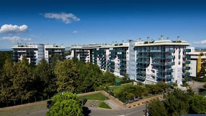 Un immeuble résidentiel moderne à plusieurs étages, doté de balcons, entouré de verdure et surplombant un ciel dégagé.