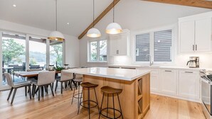 Een moderne keuken met een groot eiland, witte kasten en een zithoek met een houten tafel en barkrukken.