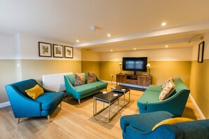 A living room with teal sofas, a coffee table, and a flat-screen TV on a wooden cabinet. - Breckland Thatched Cottage (Hockwold cum Wilton)