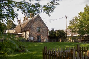 A stone building with a thatched roof, surrounded by a wooden fence and a grassy yard.