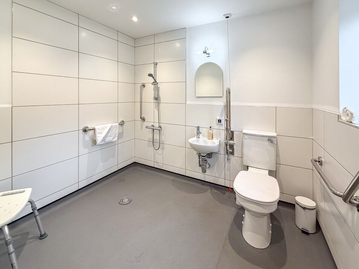 A modern bathroom with white tiles, a toilet, a sink, a shower, and a mirror.