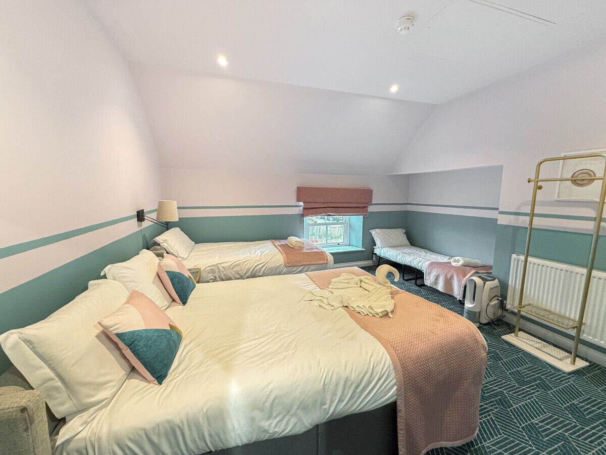 A hotel room with three beds, a window, a radiator, and a ceiling fan.