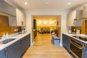 A modern kitchen with grey cabinets, a central island, and a dining area with chairs and a table. - Breckland Thatched Cottage (Hockwold cum Wilton)