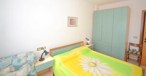 Een slaapkamer met een bed, nachtkastje, bureau, stoel, kledingkast en een aan de muur hangend schilderij.