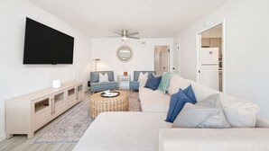 Un salon moderne doté d’un téléviseur à écran plat, de deux canapés, d’une table basse et d’un ventilateur de plafond.