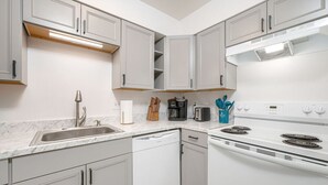 Une cuisine moderne avec des meubles blancs, un évier en acier inoxydable, un lave-vaisselle, une cuisinière et une machine à café.