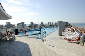 Un espace piscine aménagé sur le toit, avec des chaises longues, une piscine et une vue sur la mer.
