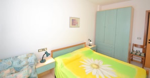 Une chambre à coucher comprenant un lit, une table de chevet, un bureau, une chaise, une armoire et un tableau accroché au mur.