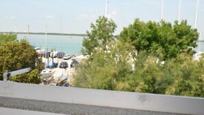 Un balcon avec une table et des chaises, donnant sur une marina où sont amarrés des bateaux, et sous un ciel dégagé.