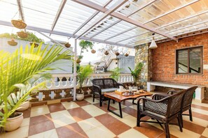 A covered patio area with checkered flooring, wicker furniture, and hanging planters. - Rahta Villa - An Elegant 3BR Villa With BBQ Terrace (Dehradun)