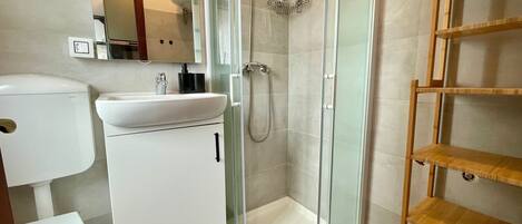 A bathroom with a toilet, sink, shower, and a glass-enclosed shower stall.
