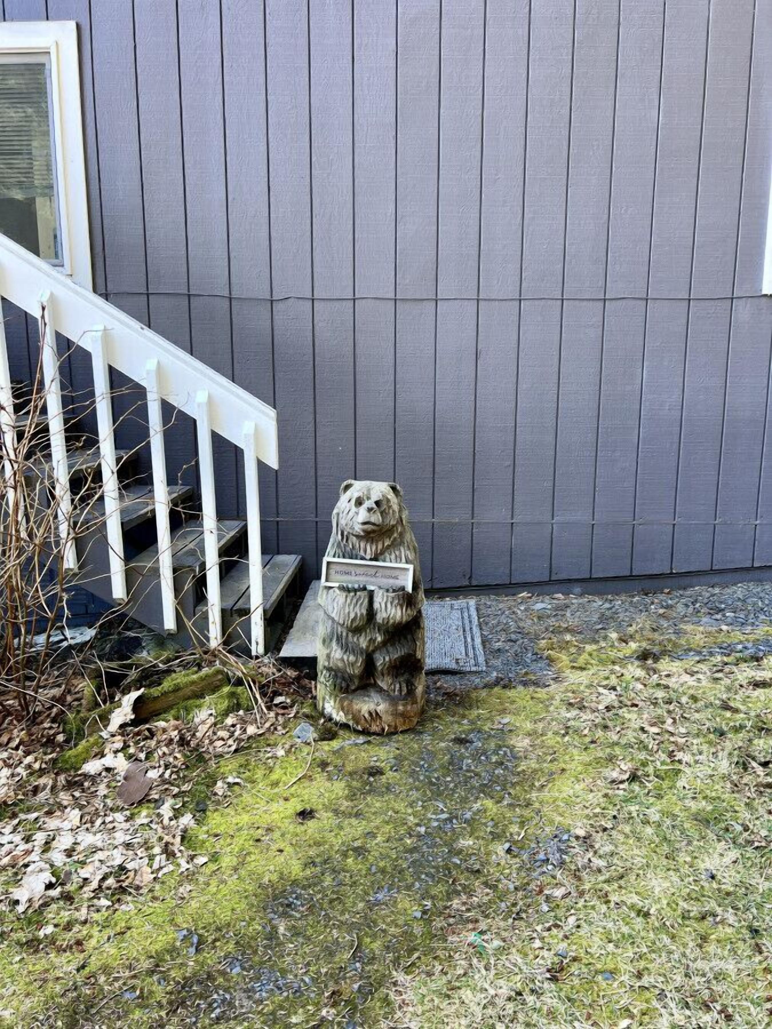 Karhusta tehty kivipatsas sijaitsee harmaan rakennuksen edessä, ja rakennuksessa on valkoinen portaikko.