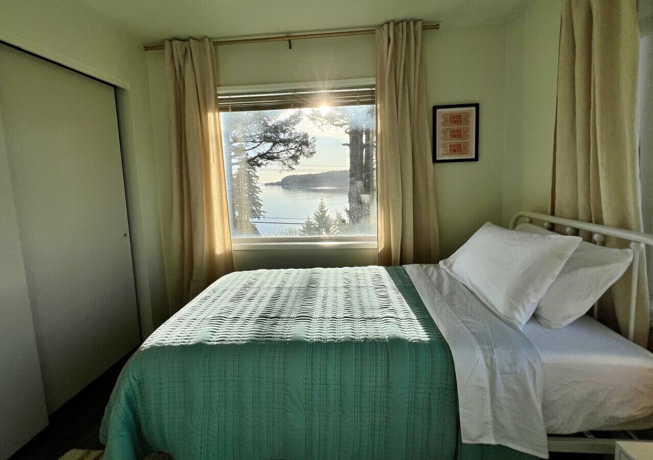 A room with a bed, a window with curtains, and a framed picture on the wall.