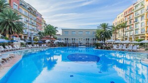A hotel pool area with multiple lounge chairs and umbrellas, surrounded by multi-story buildings with balconies. - Coberturas sofisticadas no IL Campanario Resort ILCTOPM (Florianópolis)
