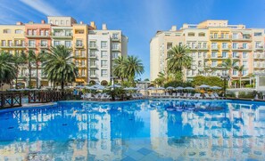 A swimming pool surrounded by palm trees and lounge chairs, with multi-story buildings in the background. - Coberturas sofisticadas no IL Campanario Resort ILCTOPM (Florianópolis)