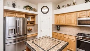 A kitchen with stainless steel appliances, wooden cabinets, a granite countertop, and a clock on the wall. - Havasu Jamaica S - Pool, Spa, Casita, Central (Lake Havasu City)