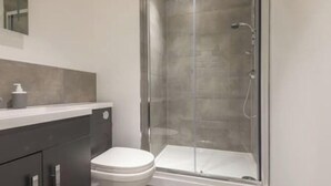 Un baño moderno con ducha envuelta en vidrio, inodoro y tocador con dispensador de jabón.