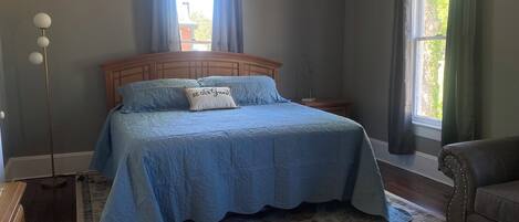 Quarto com cama grande, mesa de cabeceira, luminária de chão e vista para o exterior pela janela.