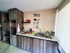 Una cocina compacta con un mueble de madera, un lavamanos y una encimera. Hay utensilios de cocina y una cafetera sobre la encimera.
