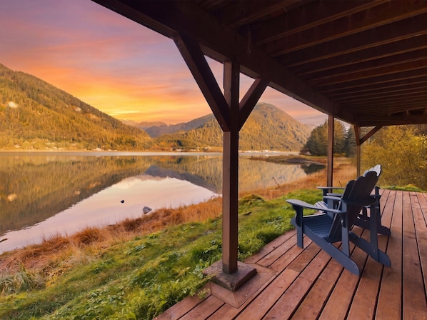 Une terrasse en bois, agrémentée de chaises Adirondack, qui offre une vue sur un lac paisible et des montagnes boisées.